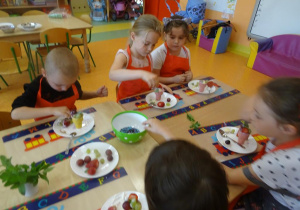 Dzieci dekorują lody w wafelku owocami.